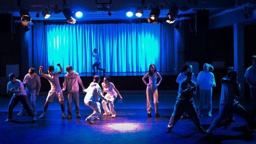 Tanzende Schüler:innen auf einer in blaues Licht getauchten Bühne.